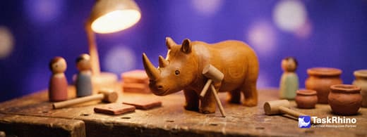 A small wooden rhino stands with a small team of wooden peg figures among finished tile boards and tools in a warm workshop.