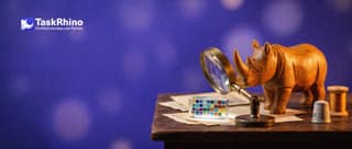 A small wooden rhino peers through a brass magnifying glass on a stand at a small block of clear glass divided into a neat grid of tiny coloured cells.