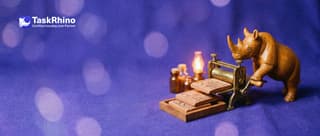 A small wooden rhino turns the crank of a tiny brass printing press that lays out three identical small tile boards in a neat stack.