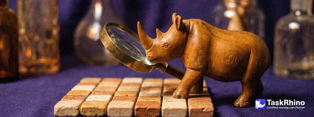 A small wooden rhino studies a tile board closely through a large brass magnifying glass.