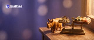 A small wooden rhino stands beside an old brass balance scale: one pan holds a complicated little brass gadget full of dials, the other holds a tidy board of coloured tiles.
