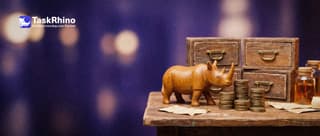A small wooden rhino stacks small brass coins into columns of different heights, each column in front of a tiny tool chest, like a bar chart made of coins.