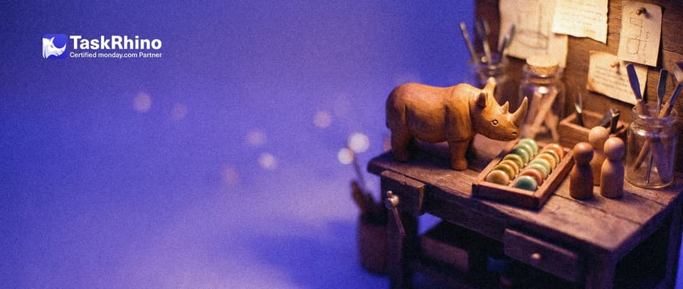 A small wooden rhino stands at a tiny shop workbench beside a tidy board of coloured tiles and three small wooden peg figures of a little team.