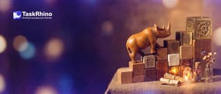A small wooden rhino climbs a staircase of ten wooden blocks that grows from a small plain block at the bottom to a large complex brass block at the top.
