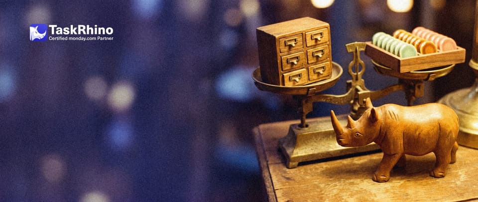 A small wooden rhino points to the heavier side of a balance scale: an old dusty card cabinet on one pan and a tidy board of coloured tiles on the other.