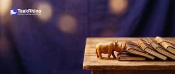 A small wooden rhino pulls one notebook out of a small wooden bookshelf full of different notebooks and journals with its horn.