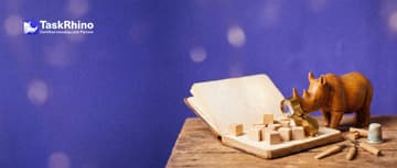 A small wooden rhino studies a large open blank notebook with small wooden building blocks stacked on its pages, holding a brass loupe.