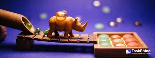 A small wooden rhino carries items from a short wooden pipe chute with green marbles rolling out into a tidy board of coloured tiles, nothing dropped on the way.