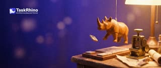 A small wooden rhino catches a duplicate tile in mid-air before it lands on a tile board beneath a small brass stamping machine.