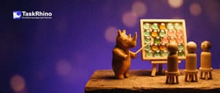 A small wooden rhino points with a little wooden pointer at a tidy board of coloured tiles on an easel while three wooden peg students watch.