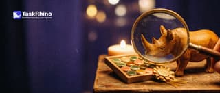 A small wooden rhino inspects a tidy board of coloured tiles through a large brass magnifying glass, a small gold rosette ribbon beside it.