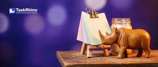 A small wooden rhino leafs through a fan of paper grid sheets in different pastel tints clipped to a little wooden easel.