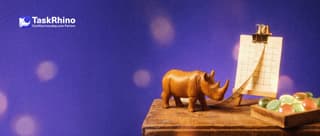 A small wooden rhino stretches a small cloth measuring tape between a paper grid sheet on a wooden easel and a tidy board of coloured tiles.