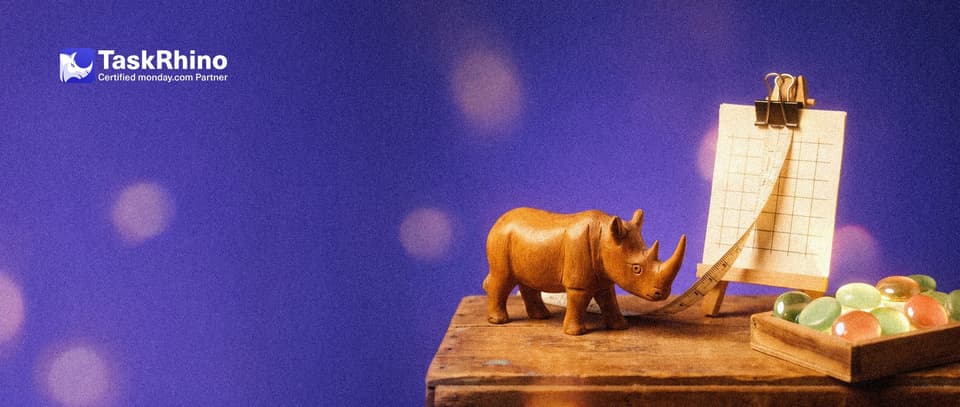 A small wooden rhino stretches a small cloth measuring tape between a paper grid sheet on a wooden easel and a tidy board of coloured tiles.