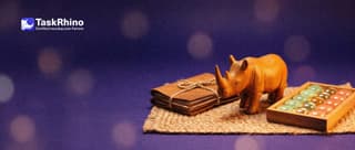 A small wooden rhino stands between a little stack of client folders tied with string and a tidy board of coloured tiles, on a woven rug.