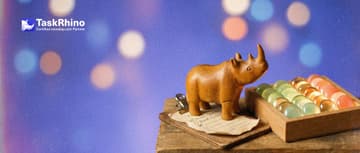 A small wooden rhino stands on a small clipboard holding a short paper checklist, looking up at a tidy board of coloured tiles beside it.