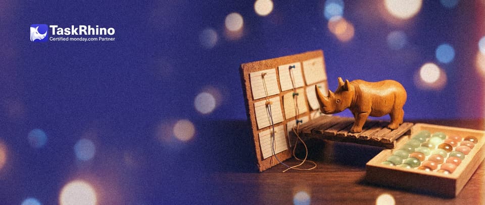 A small wooden rhino stands on a tiny wooden bridge between a cork board of index cards in columns and a tidy board of coloured tiles.