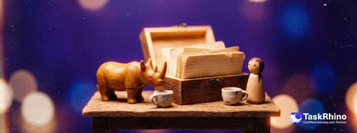 A small wooden rhino sits across a small table from a wooden peg figure, an open wooden crate of index cards between them and two teacups.