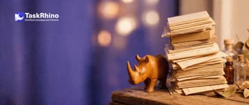 A small wooden rhino braces a huge towering, wobbling stack of paper form cards with its body.