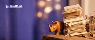 A small wooden rhino braces a huge towering, wobbling stack of paper form cards with its body.