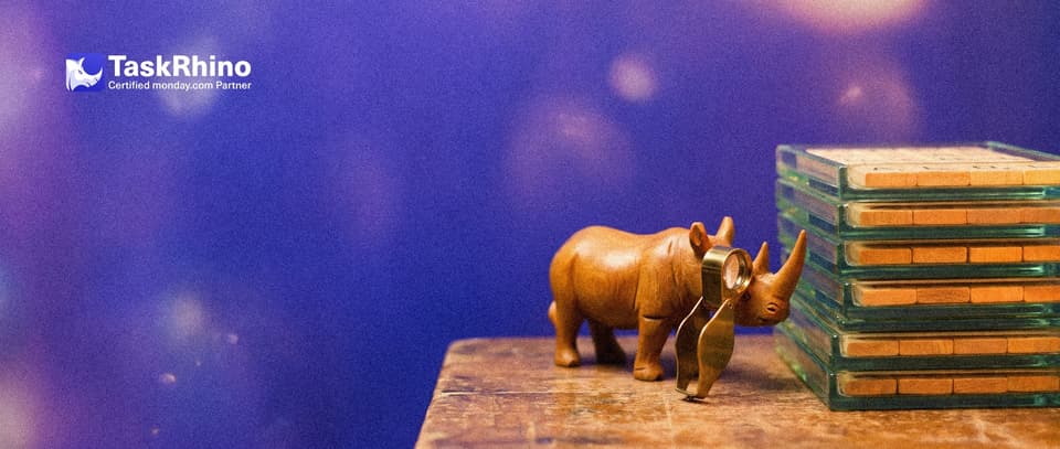 A small wooden rhino studies a tall neat stack of green-tinted glass trays holding task cards through a brass loupe.