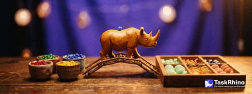 A small wooden rhino carries items from four small coloured cups of beads in red, green, blue and yellow into a tidy board of coloured tiles, nothing dropped on the way.